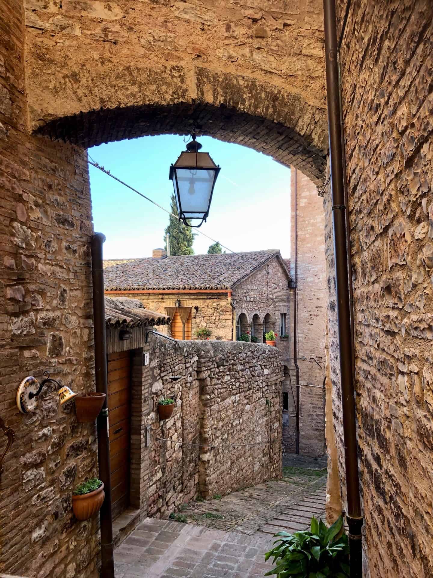 a typical medieval street in Spello with an archway, a lantern and old brick walls. 