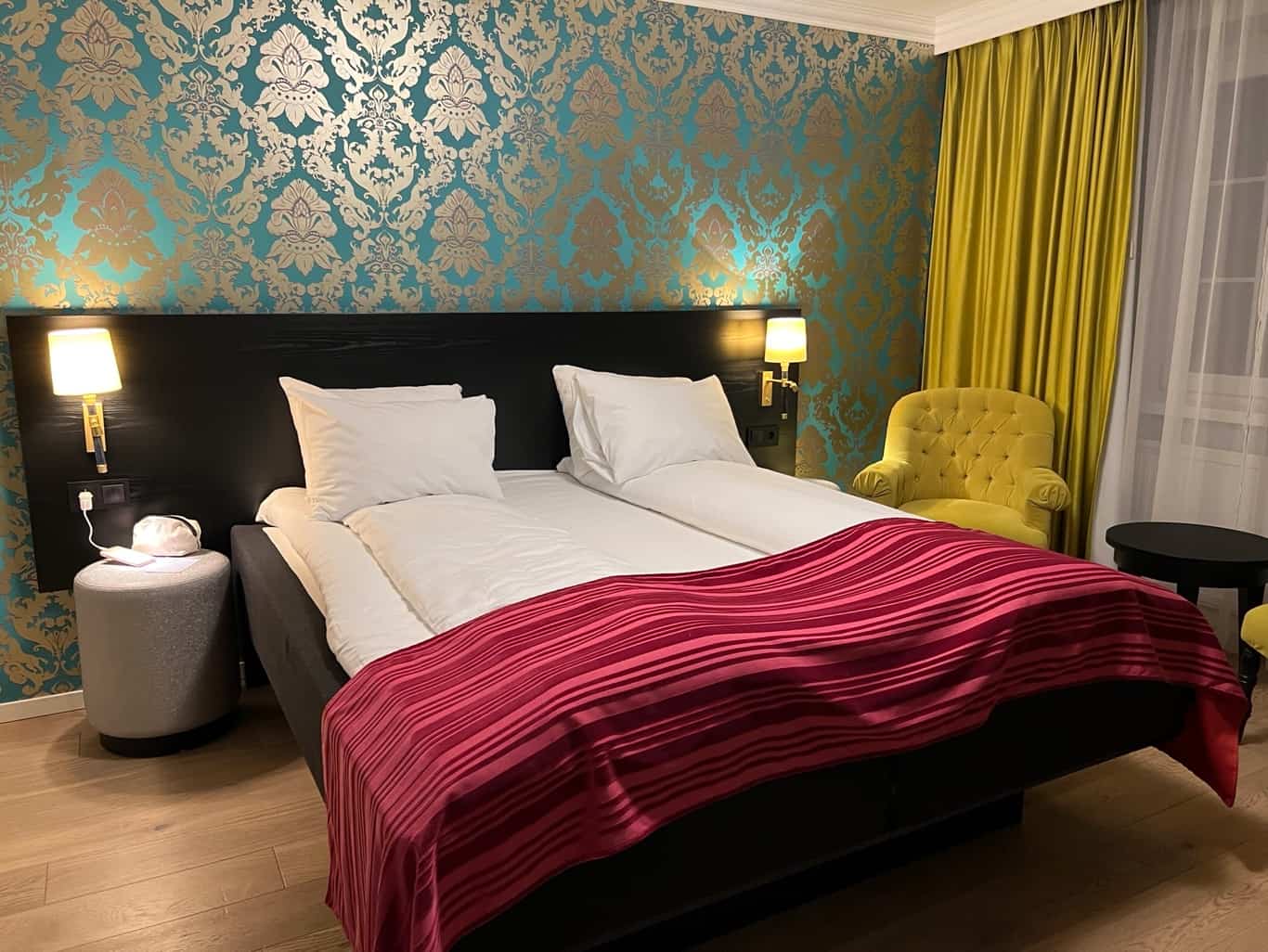 Bedroom with bed - white sheets and pillows and a red blanket and a yellow armchair. Example of a bedroom at the Thon Hotel Rosenkrantz in Bergen