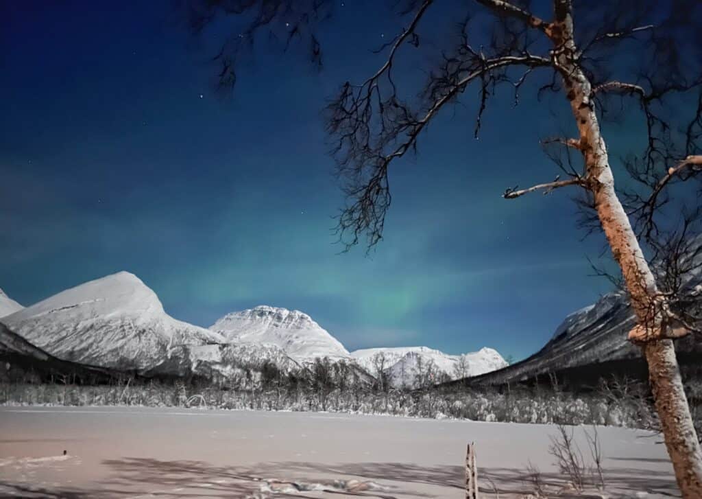 snowy mountains with a glimpse of the northern lights in the background