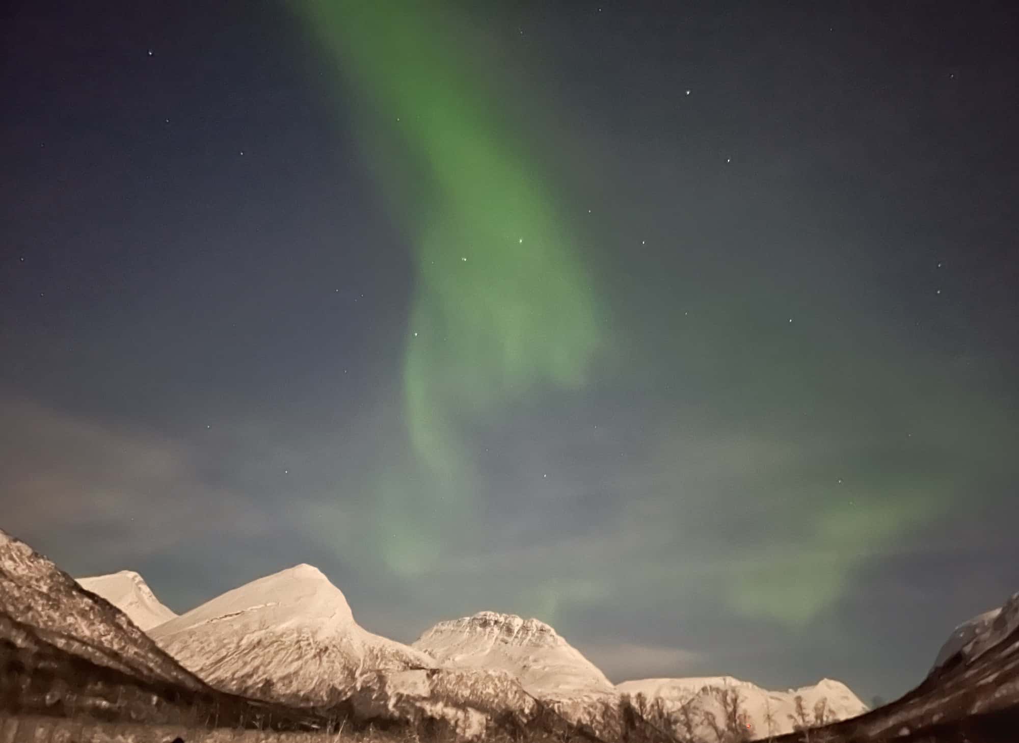 Northern lights behind snowy mountains.
