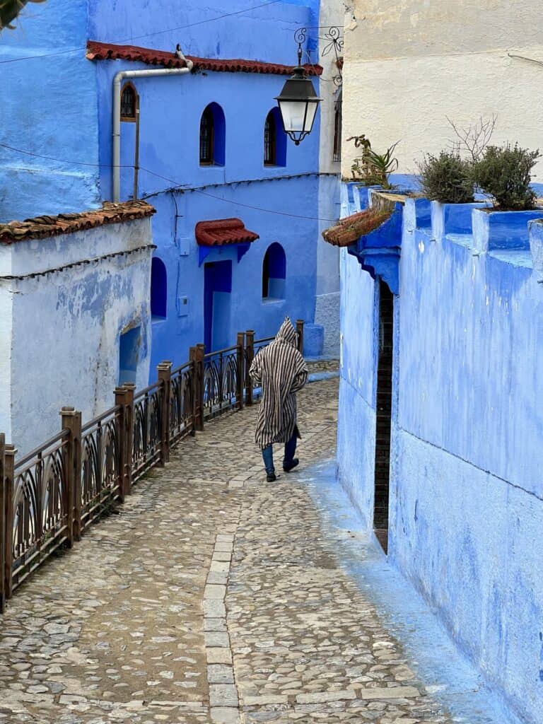 A man walking down a cobbled street lined with blue houses in Chefchaouen 