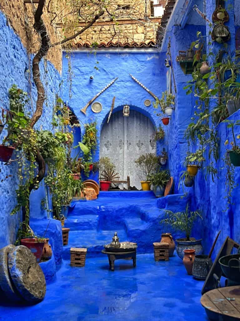 A courtyard painted in blue with plants, table and pots. 