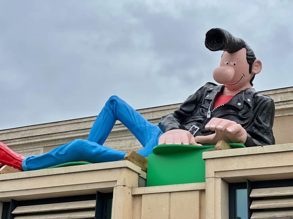 A cartoon figure of a man with a 50s quiff, black leather jacket, blue jeans, red shoes on the roof of Angouleme's train station