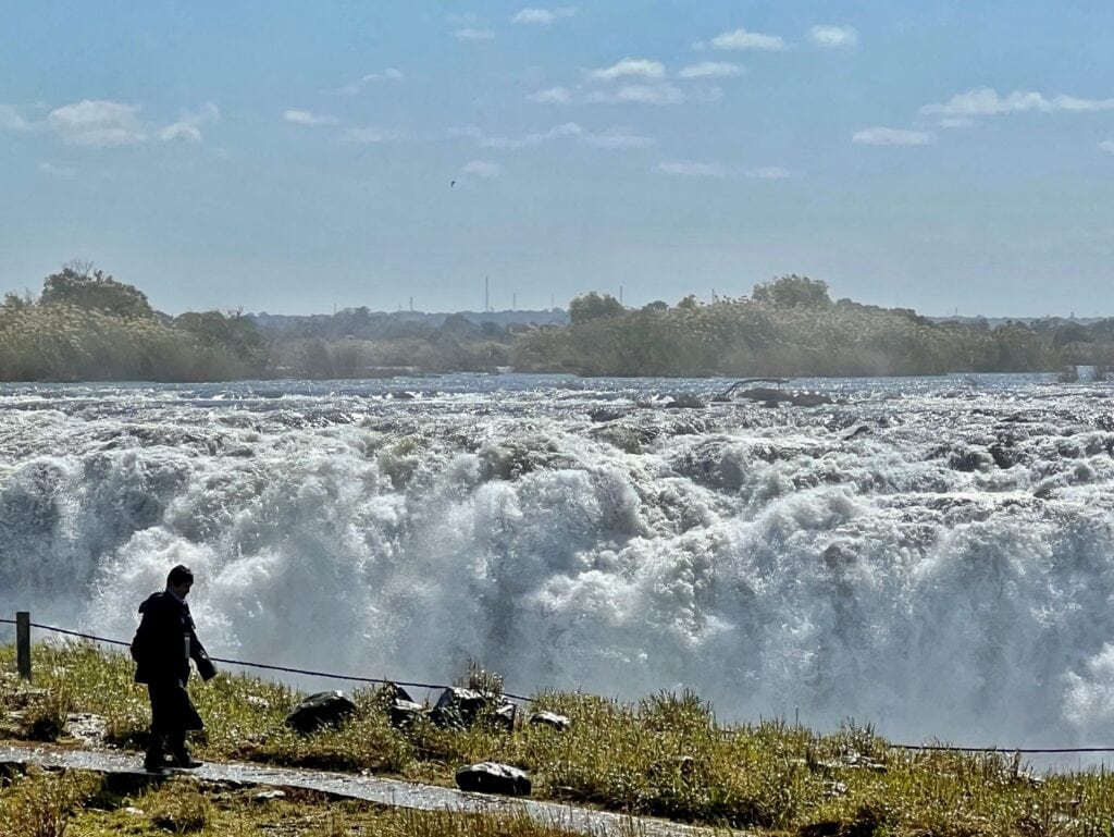 Victoria Falls in background with a man walking in the foreground