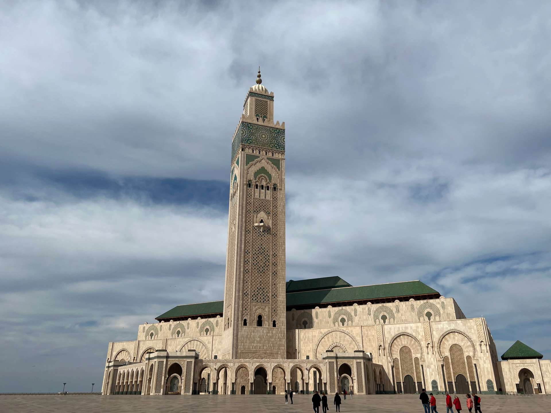 The Hassan II Casablanca Mosque facade with a very tall minaret with a cloudy sky.
