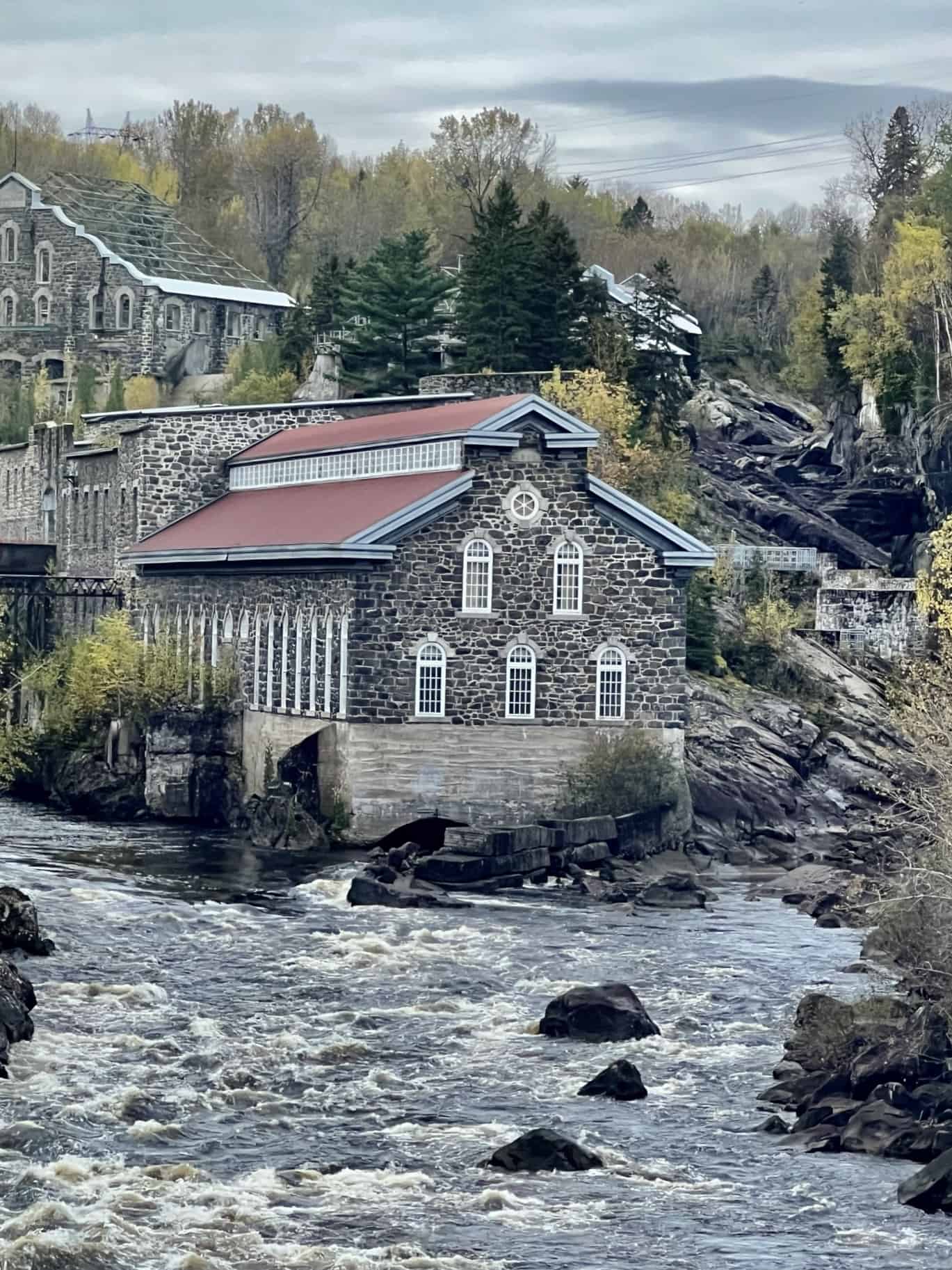 Old Chicoutimi Pulp Mill surrounded by trees and river