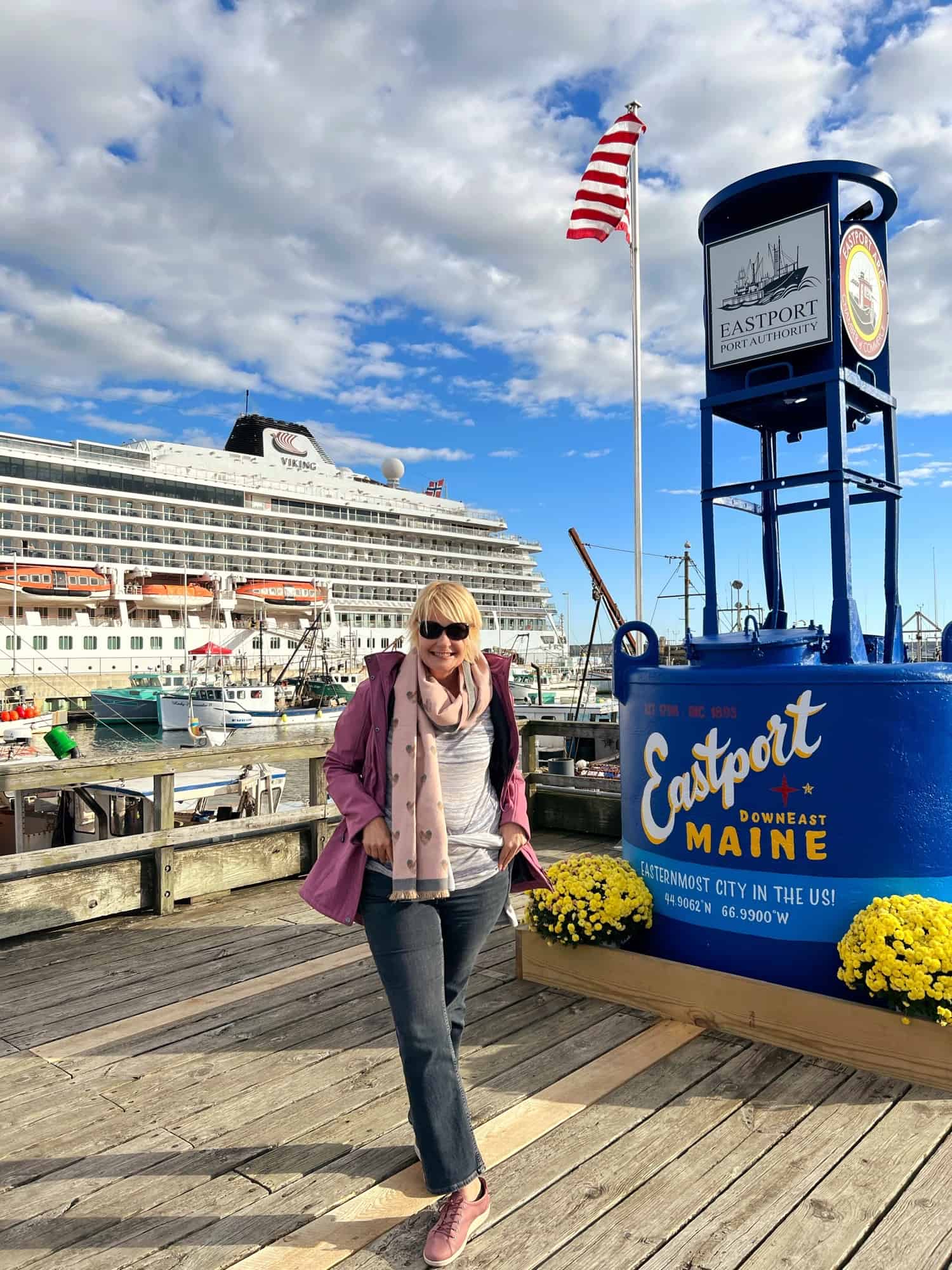 Woman standing by sign saying Eastport Maine with cruise ship in background on cruise from Montreal to Fort Lauderdale