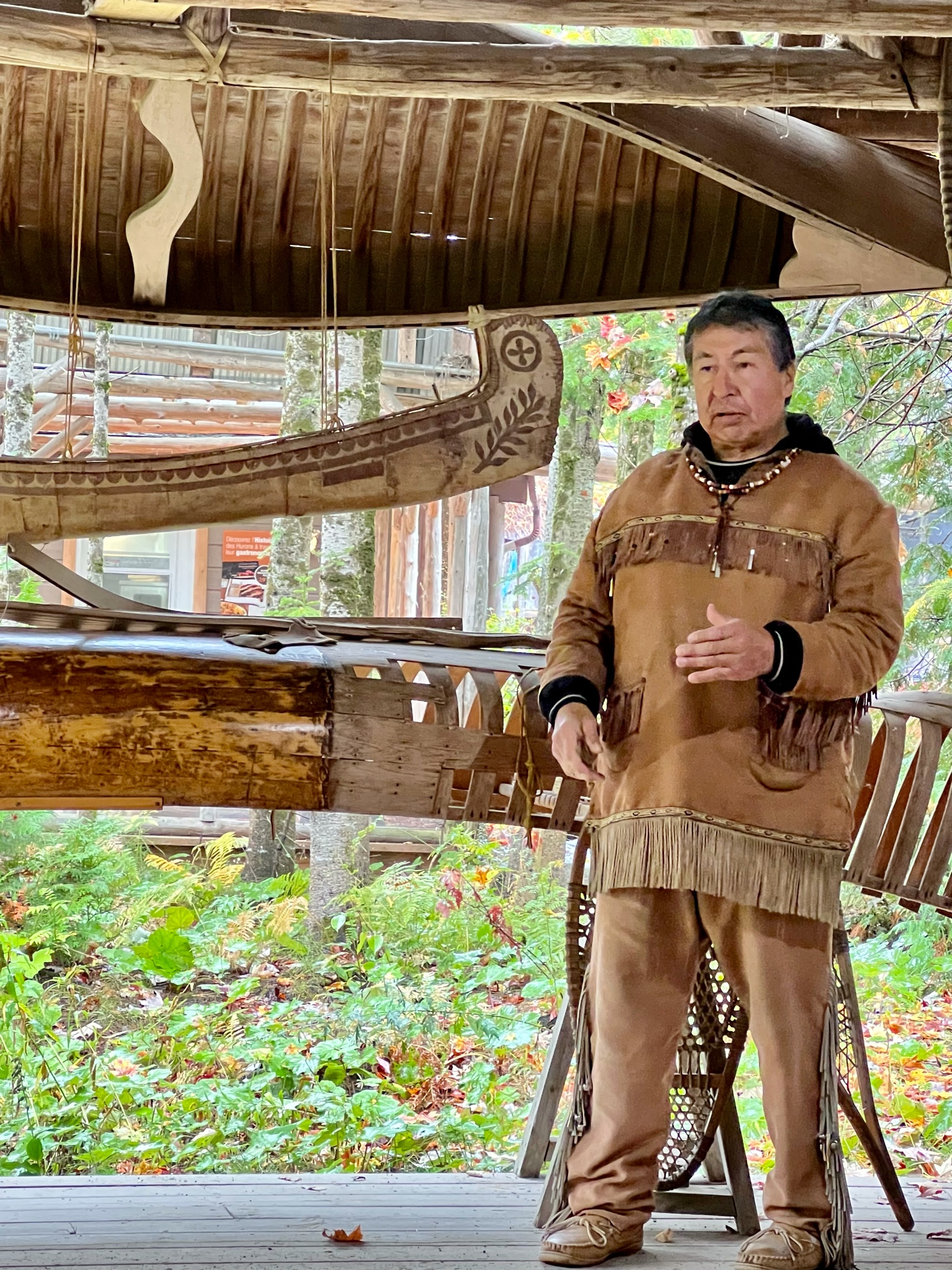 Guide wearing First Nations clothes in front of canoes