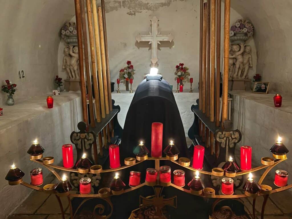 coffin surrounded by red candles and a large white cross on the wall