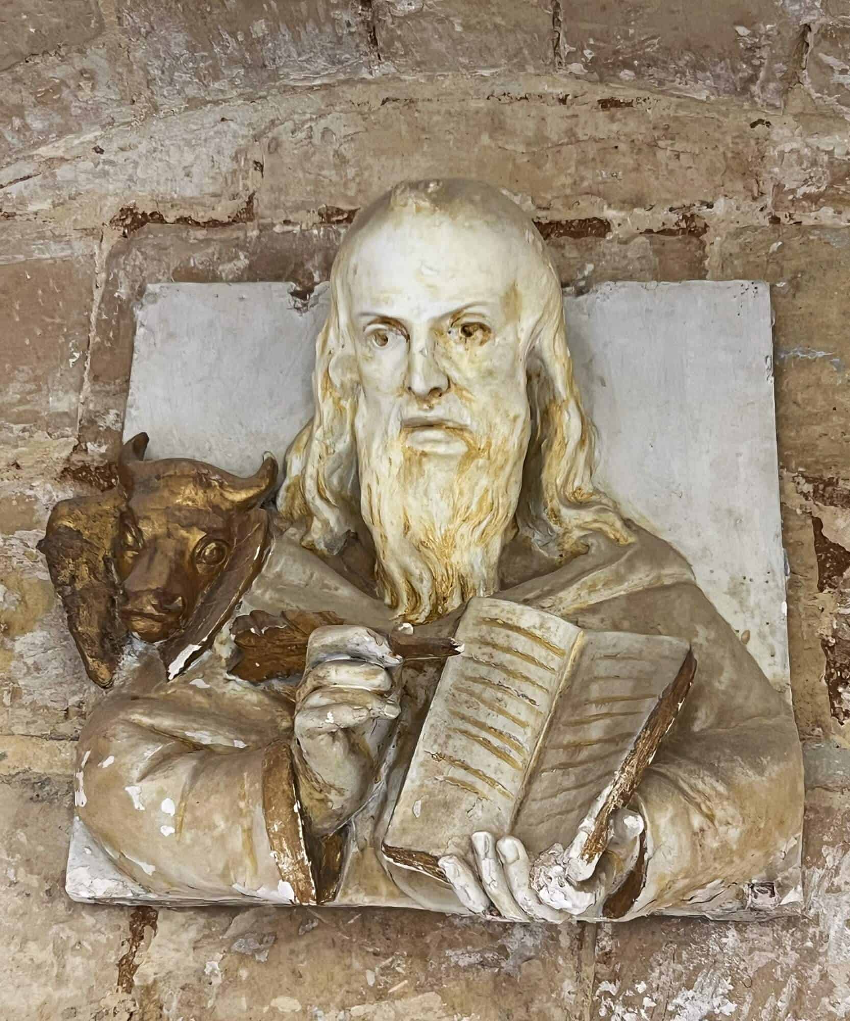 Statue on wall. Man with long beard writing in a book 