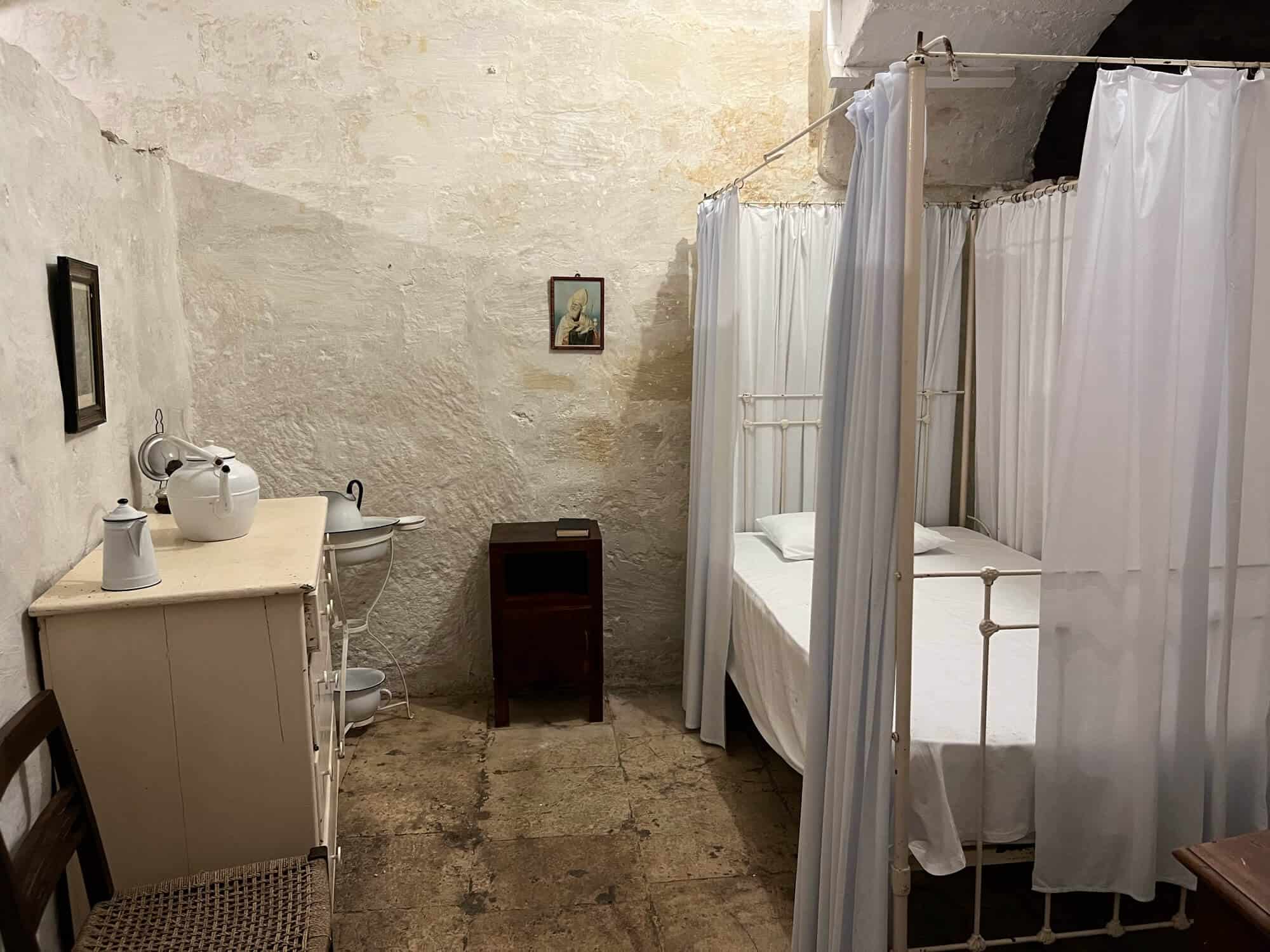 Bedroom with bed surrounded by white curtains, a desk with washing facilities. 