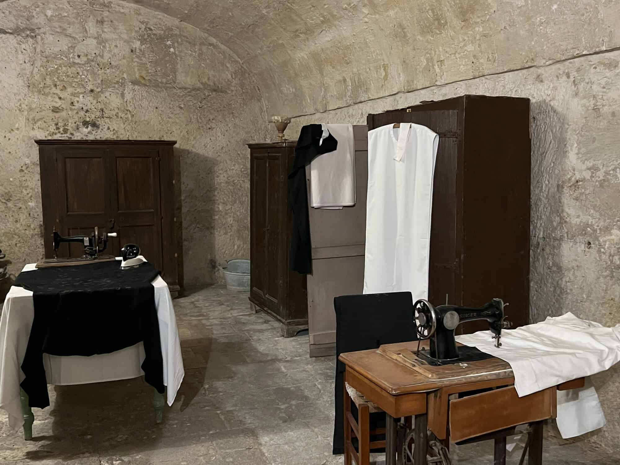 Room with sewing machine, nun's habit hanging on a wardrobe and an old steam iron
