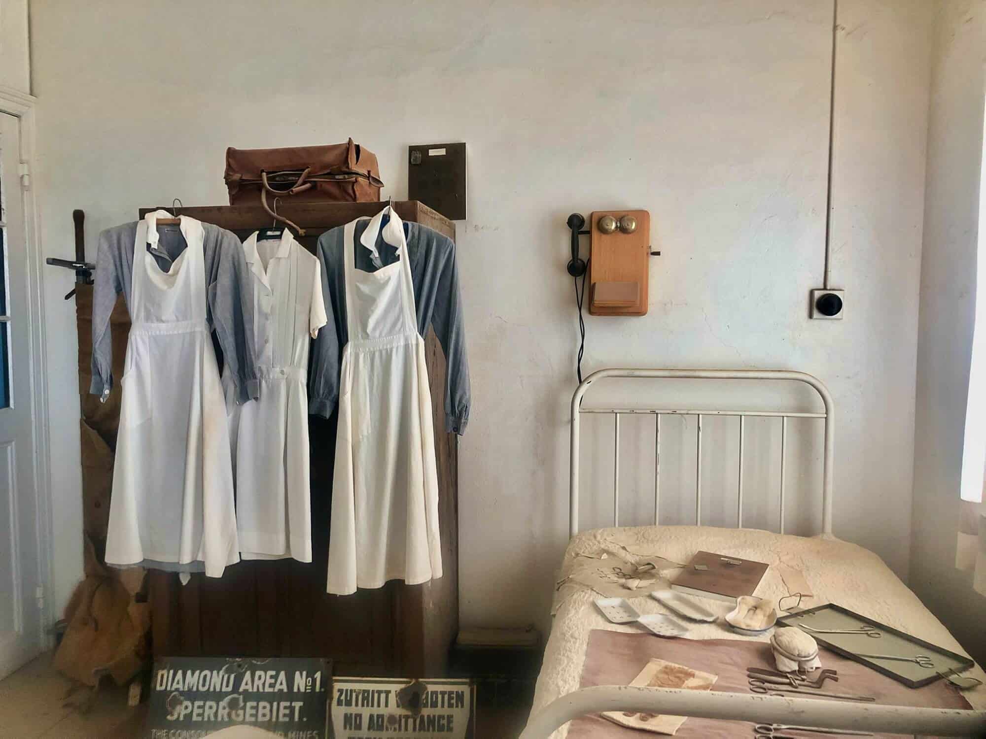 inside the hospital. 3 nurses uniform hang. A single bed with doctor's instruments and an old telephone. 
