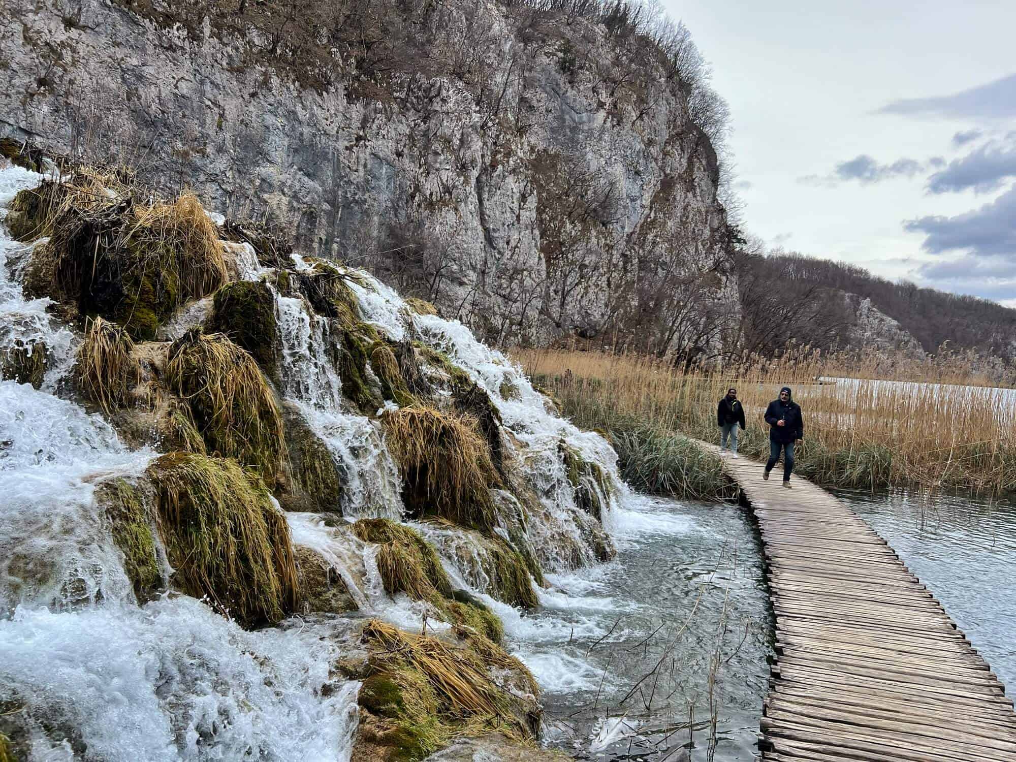 2 men walk across the lake on a wooden boardwalk 