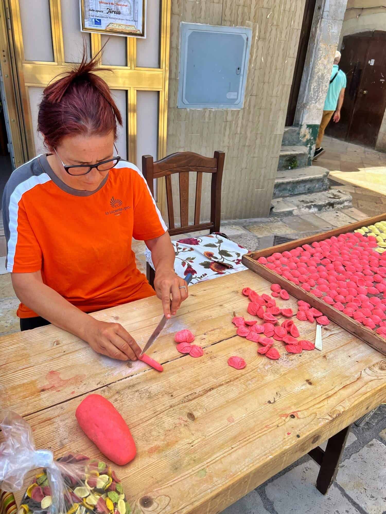 Lady wearing orange t-shirt making fresh pink coloured pasta 