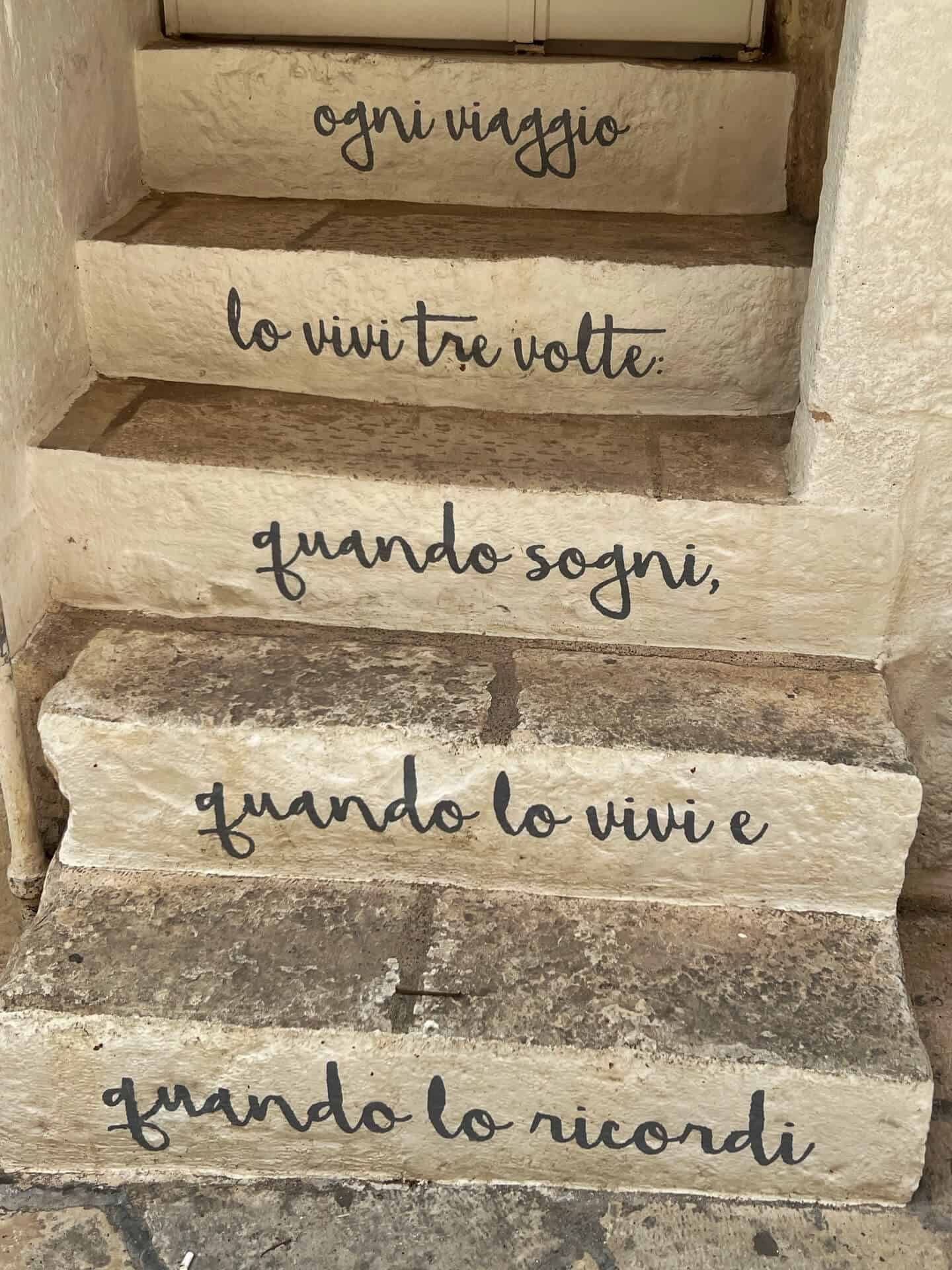 A poem in Italian written on some steps which in English reads as Each trip you live it three times: when you dream, when you live it and when you remember it