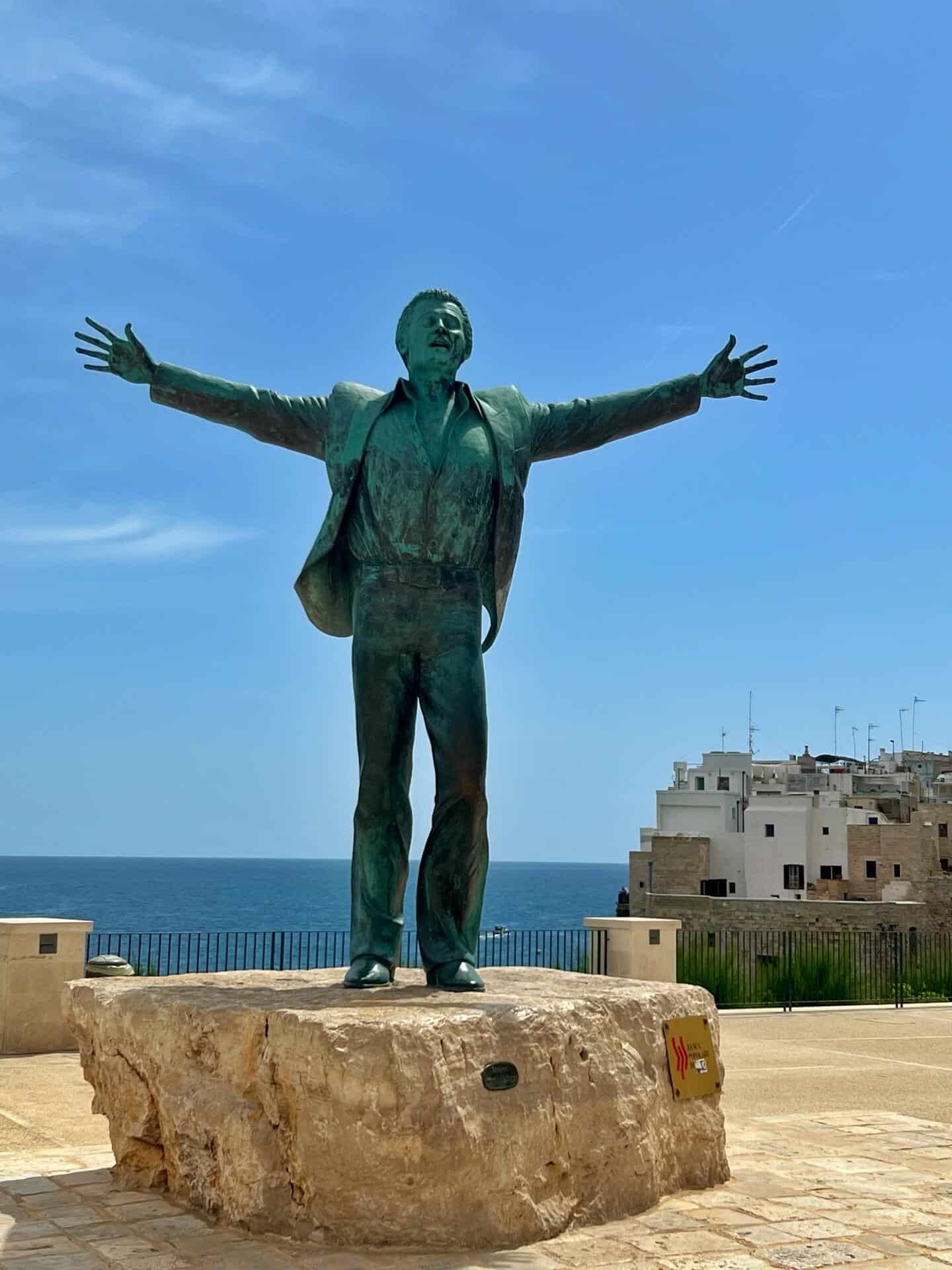 The statue of Domenico Modugno with his arms outstretched against the blue sky 