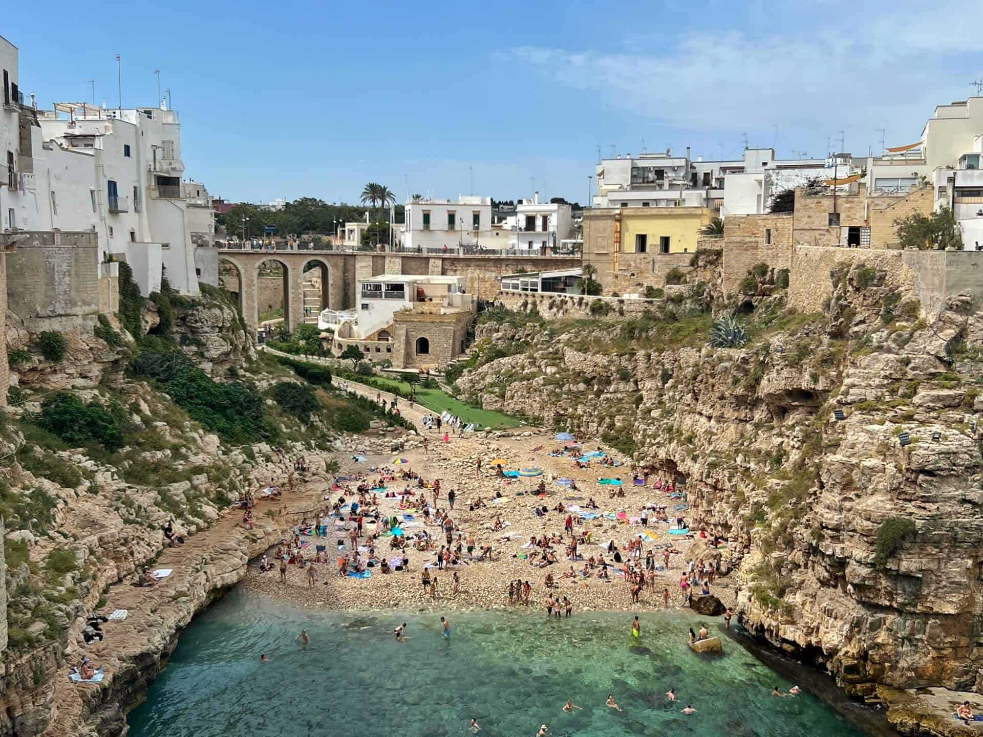 the pebbly beach filled with sunbathers between two cliffs 