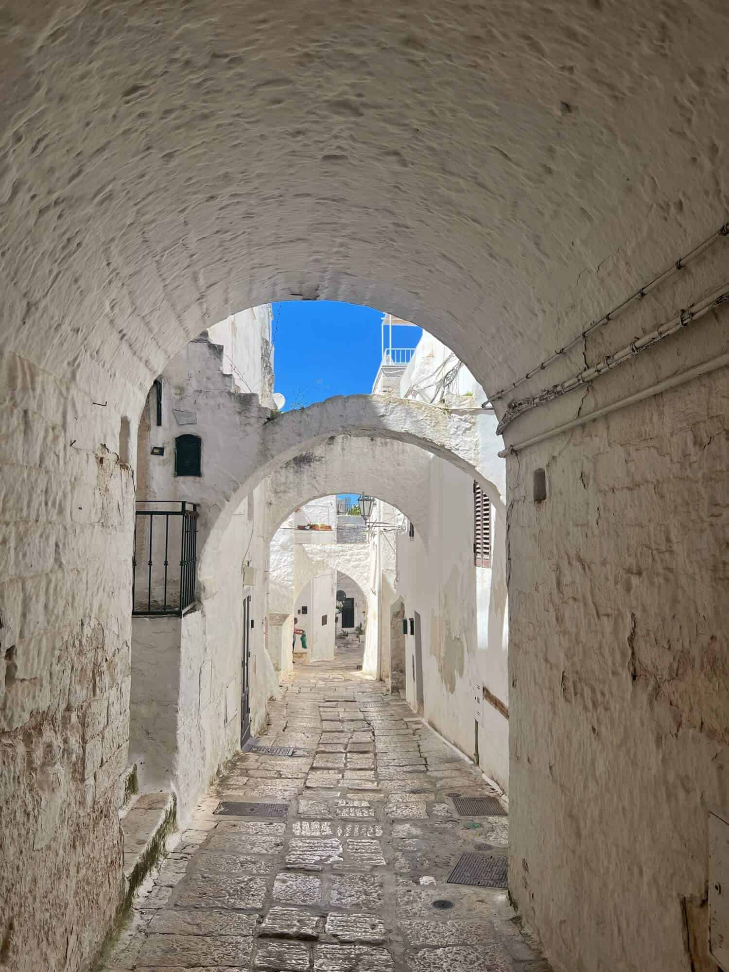 a street in Ostuni with white archways and white buildings beneath a bright blue sky 