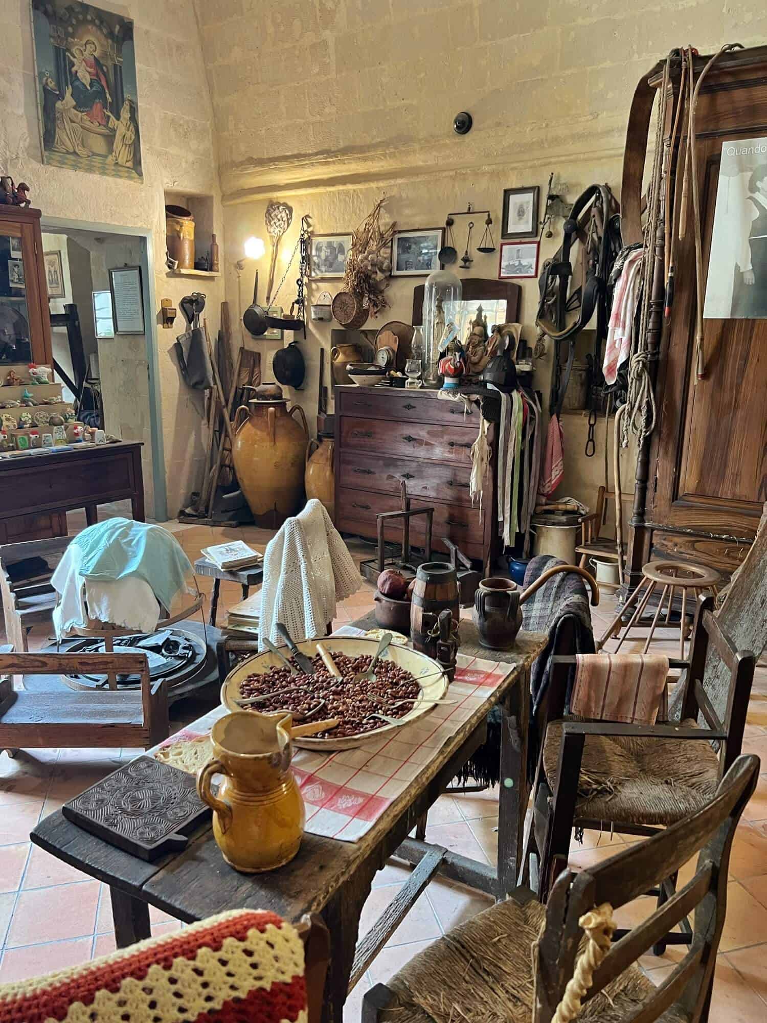 Inside the peasant museum in Matera. Table in foreground with berries and a jug. clothes in background.
