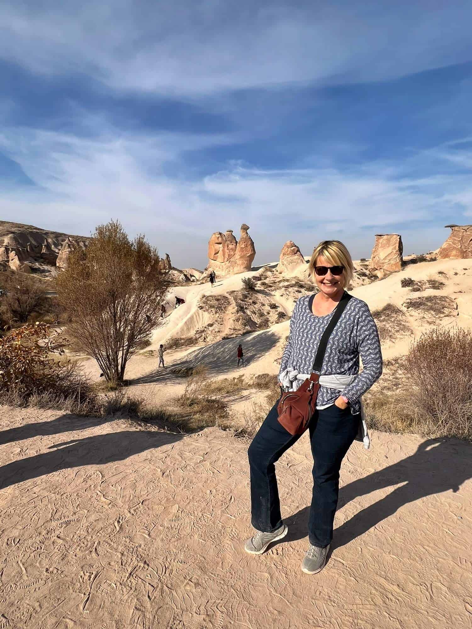 Blonde woman standing in front of a rock formation that resembles a camel 