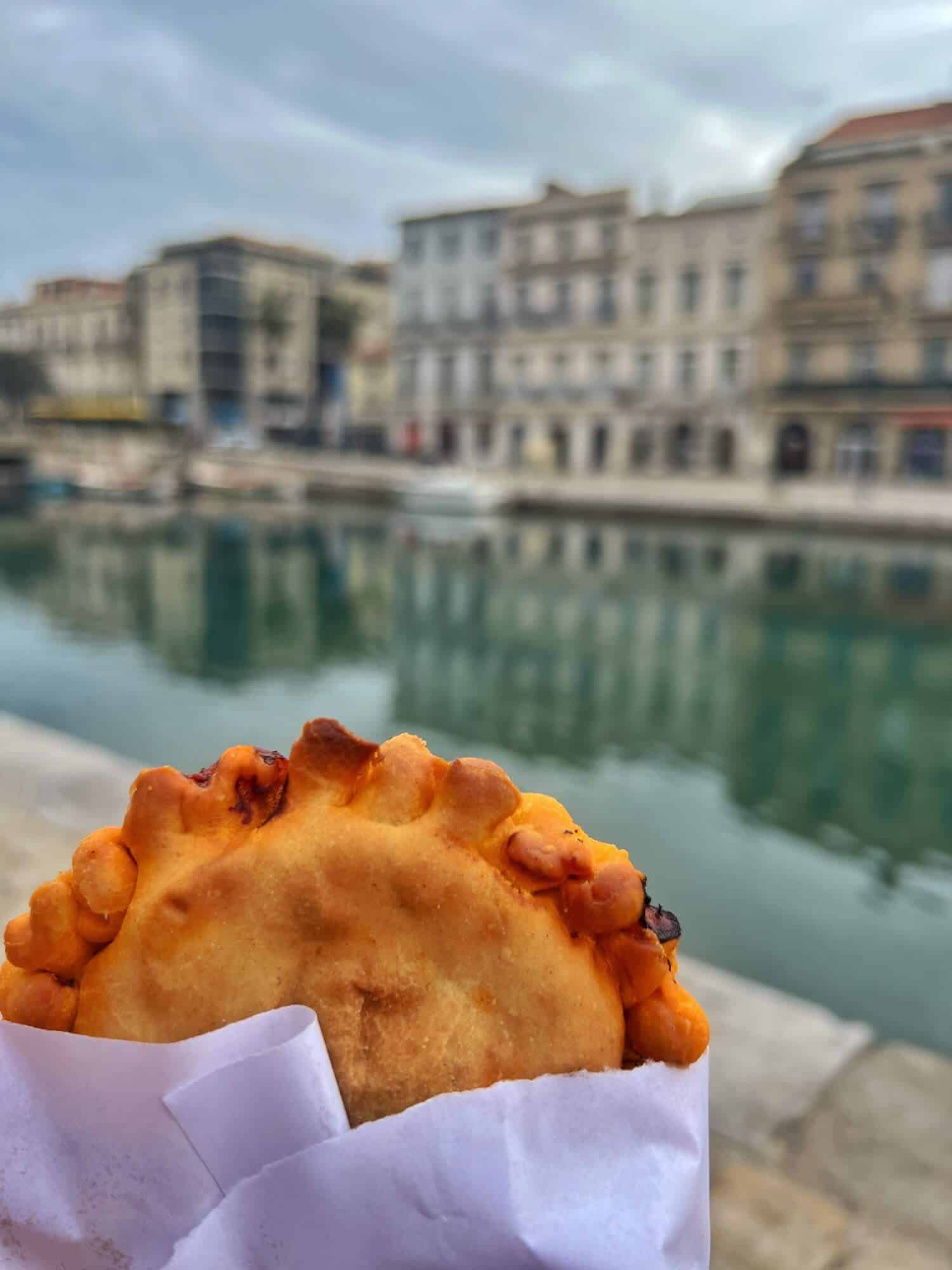 an octopus pie in a paper wrapper with the canal and houses in background 