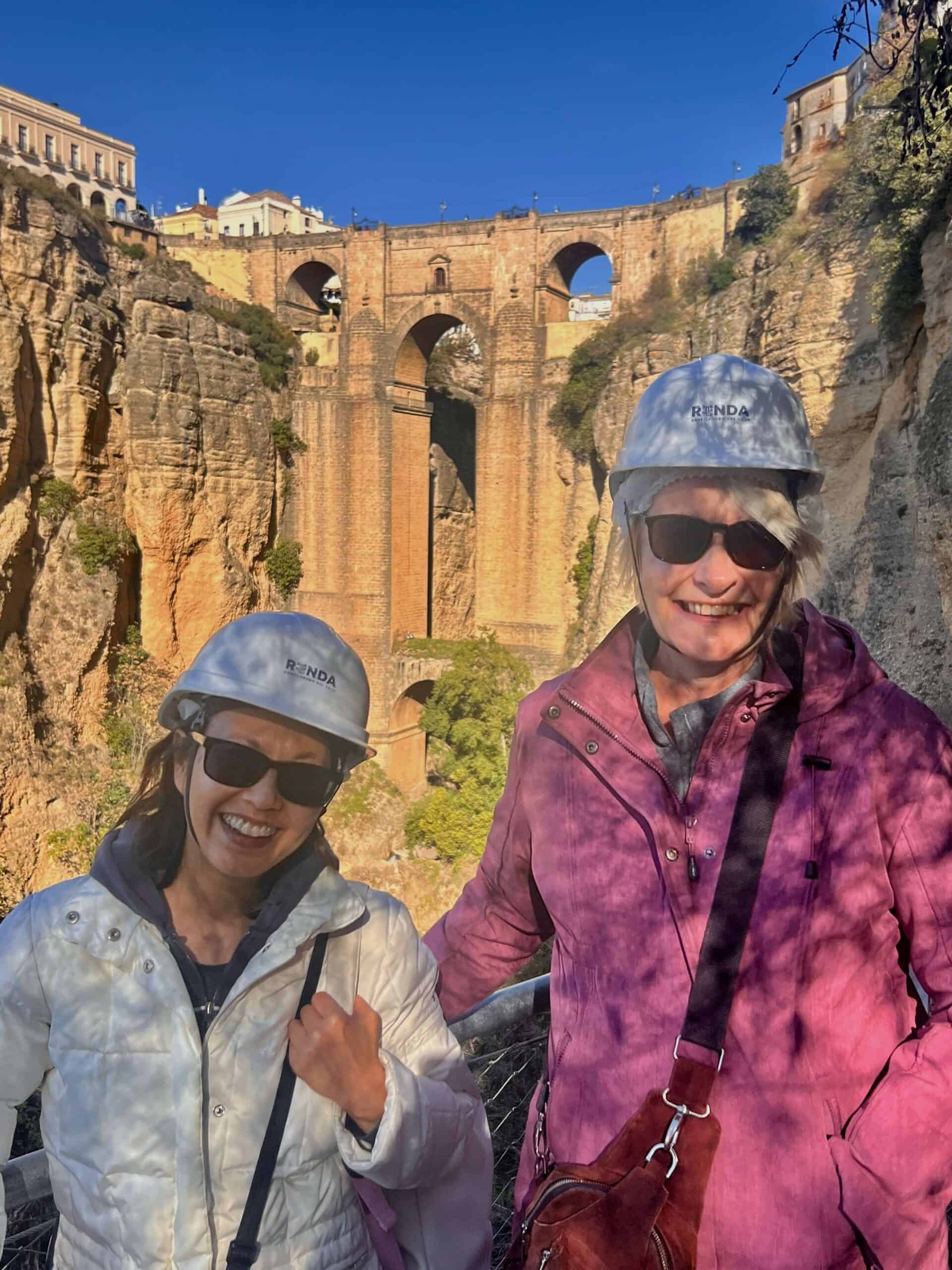 Two ladies wearing hard hats with their photo taken in front of Ronda bridge 
