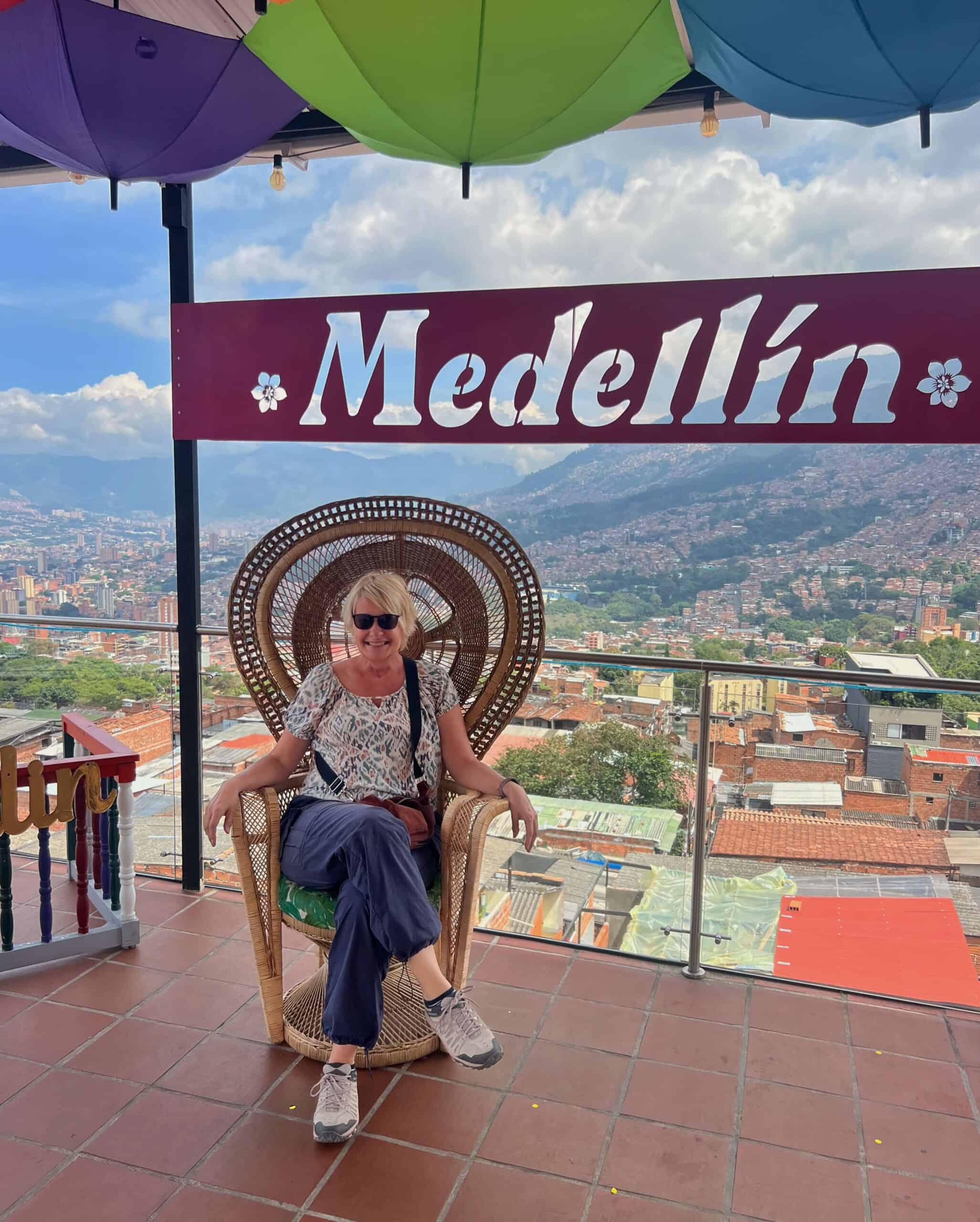 Lady sitting on a chair with the backdrop of Medellin beneath a sign