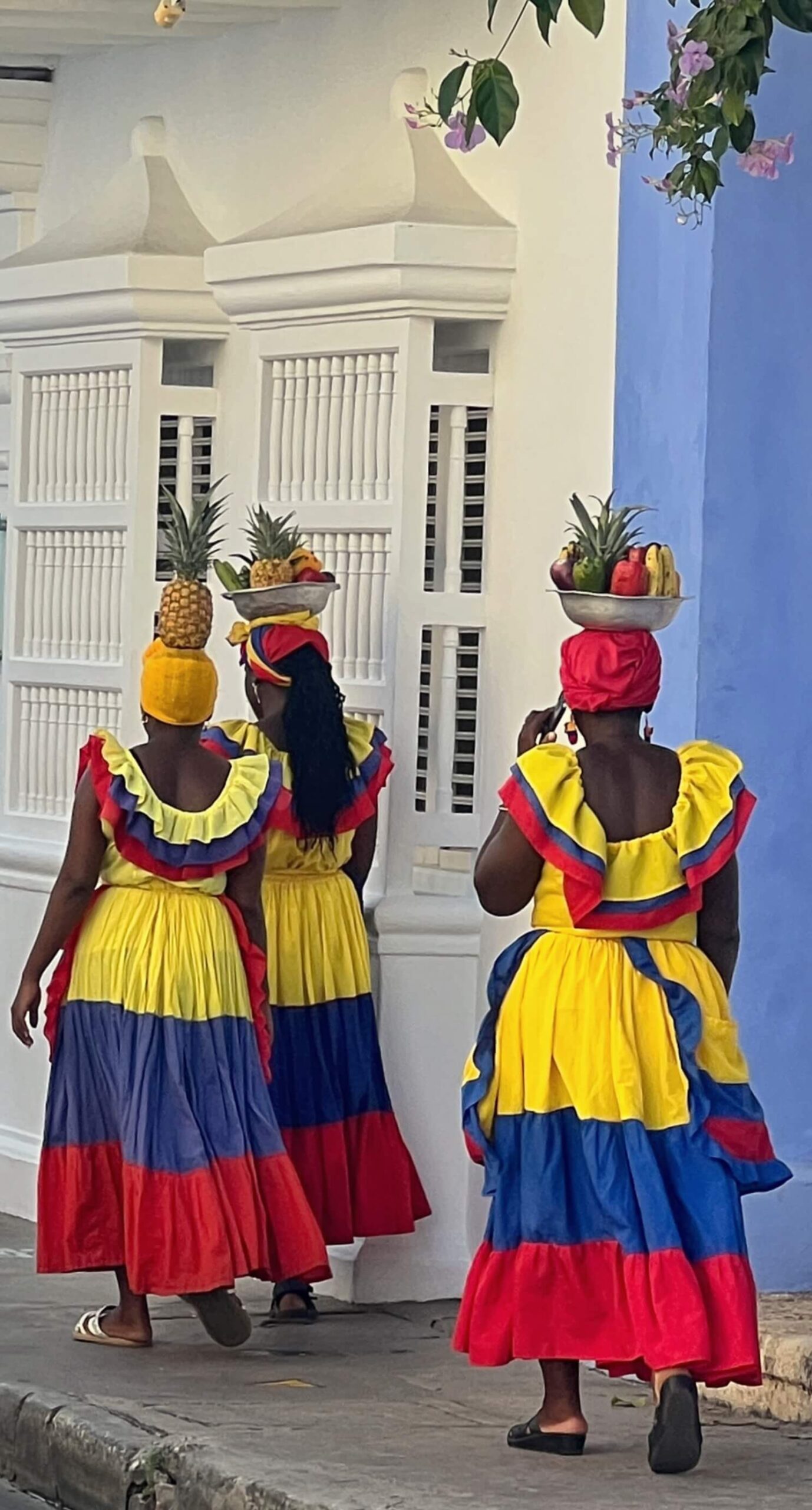 3 ladies in traditional Colombian dress with fruit baskets on their head